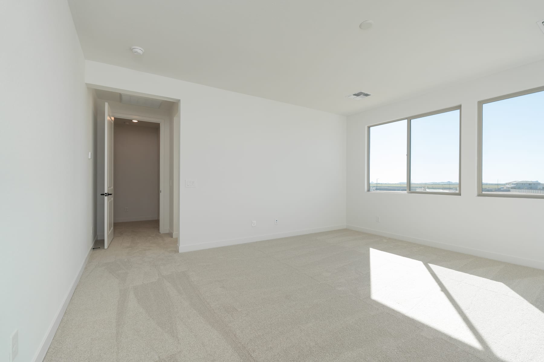 A bright and spacious room with a large window, a plain white wall, and a doorway leading to another room.