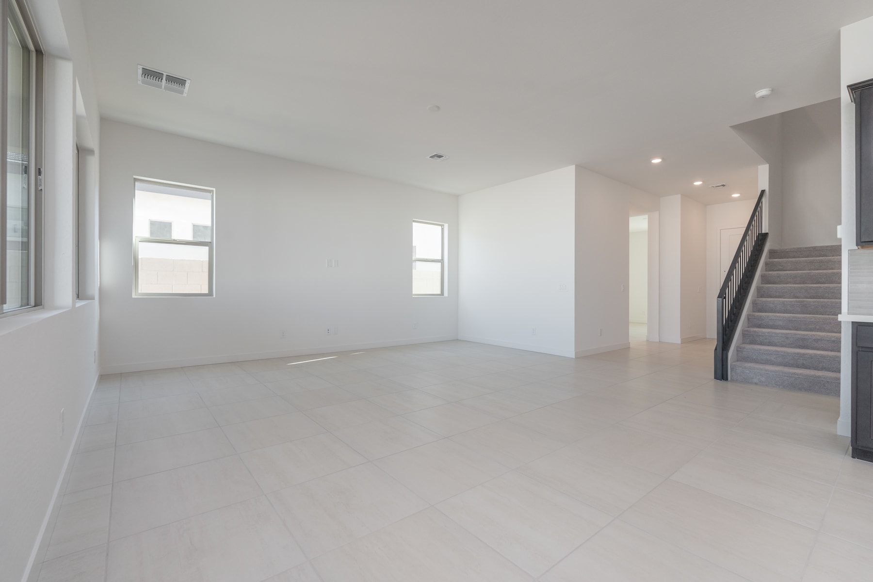 A spacious, minimalist interior with white walls, a hardwood floor, and a staircase visible in the background.