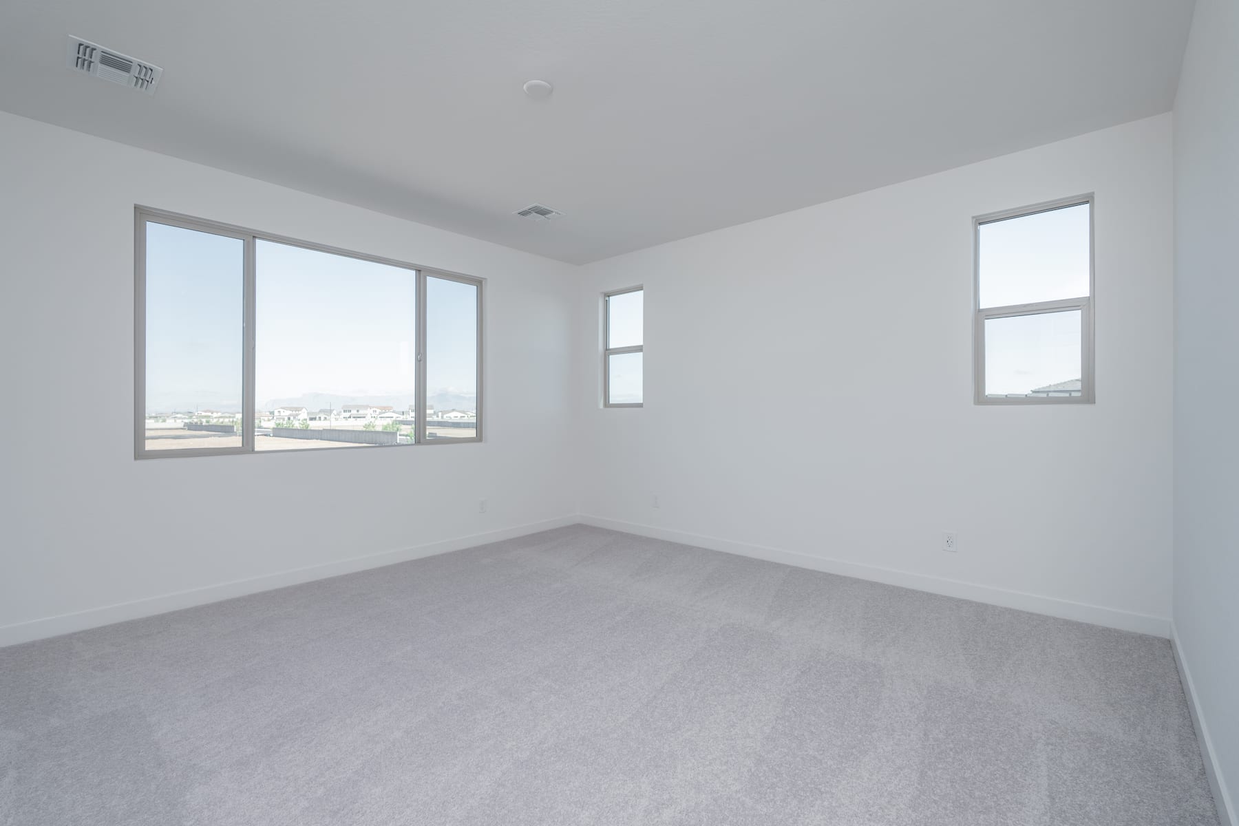 A spacious, minimalist room with large windows providing ample natural light and a view of the cityscape in the background.