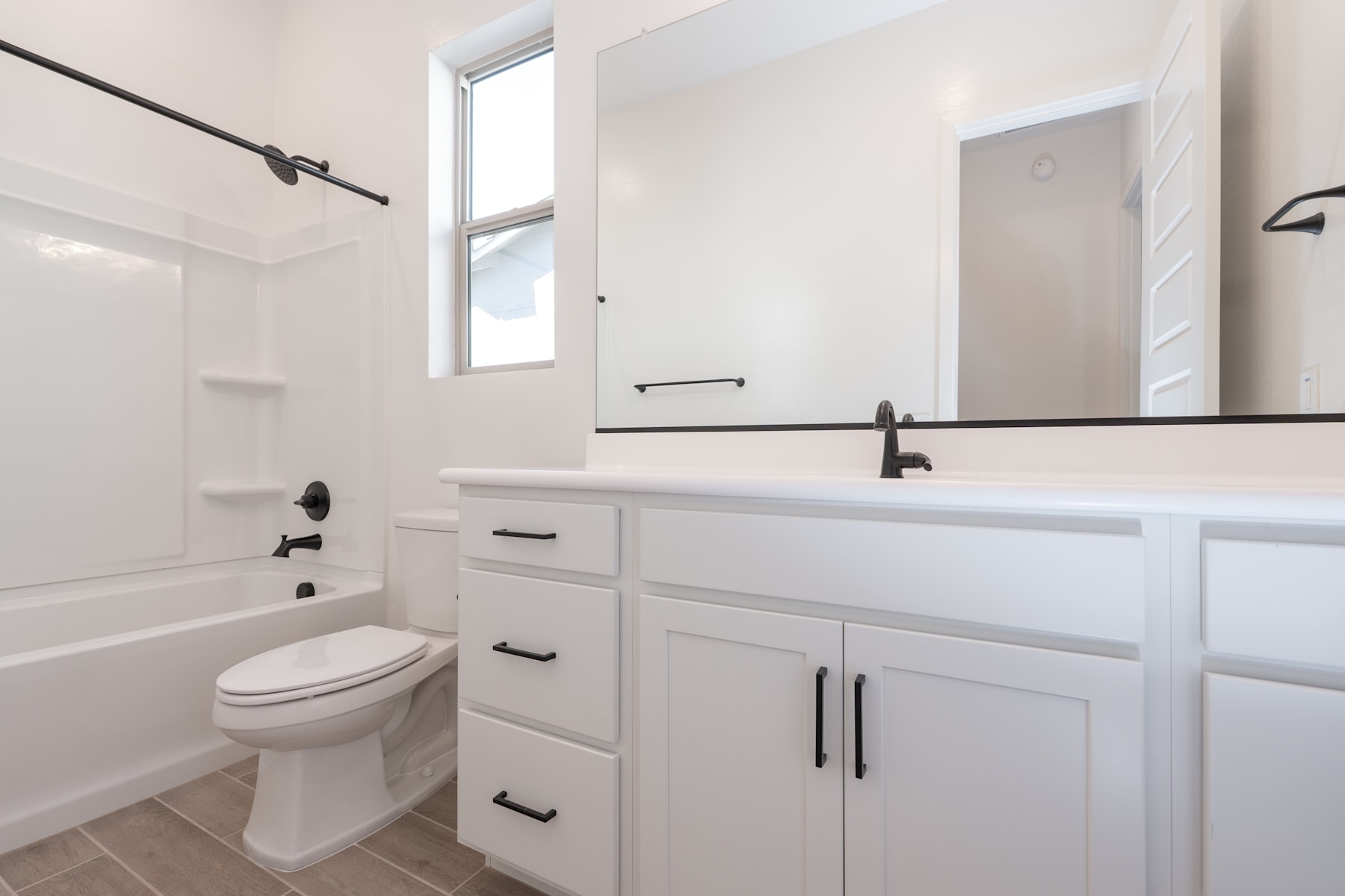 A modern, minimalist bathroom with a white vanity, toilet, and large window, creating a bright and clean atmosphere.