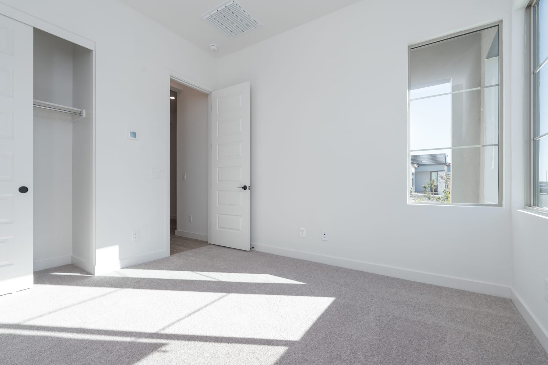 A bright, minimalist room with white walls, a large window, and a carpeted floor, creating a clean and spacious atmosphere.
