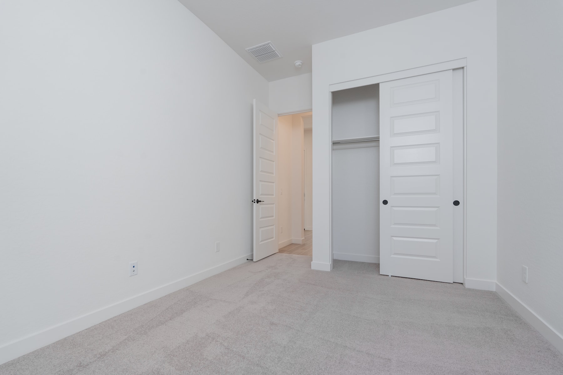 A simple, minimalist bedroom with white walls, a closet, and a carpeted floor.