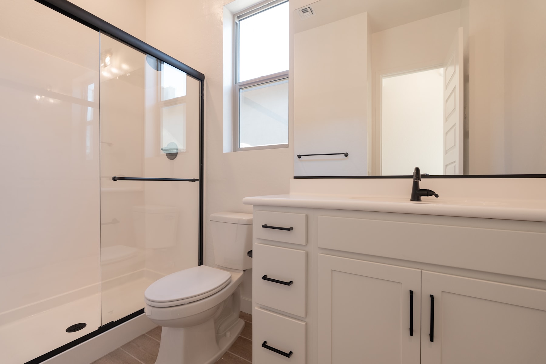 A modern and minimalist bathroom with a white vanity, a toilet, and a glass shower enclosure, all set against a neutral color palette.