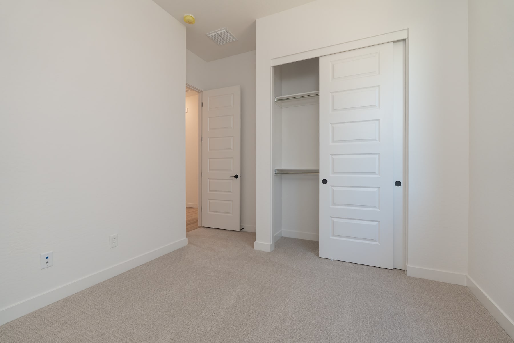 A spacious, well-lit room with white walls, a carpeted floor, and two closet doors in the foreground.