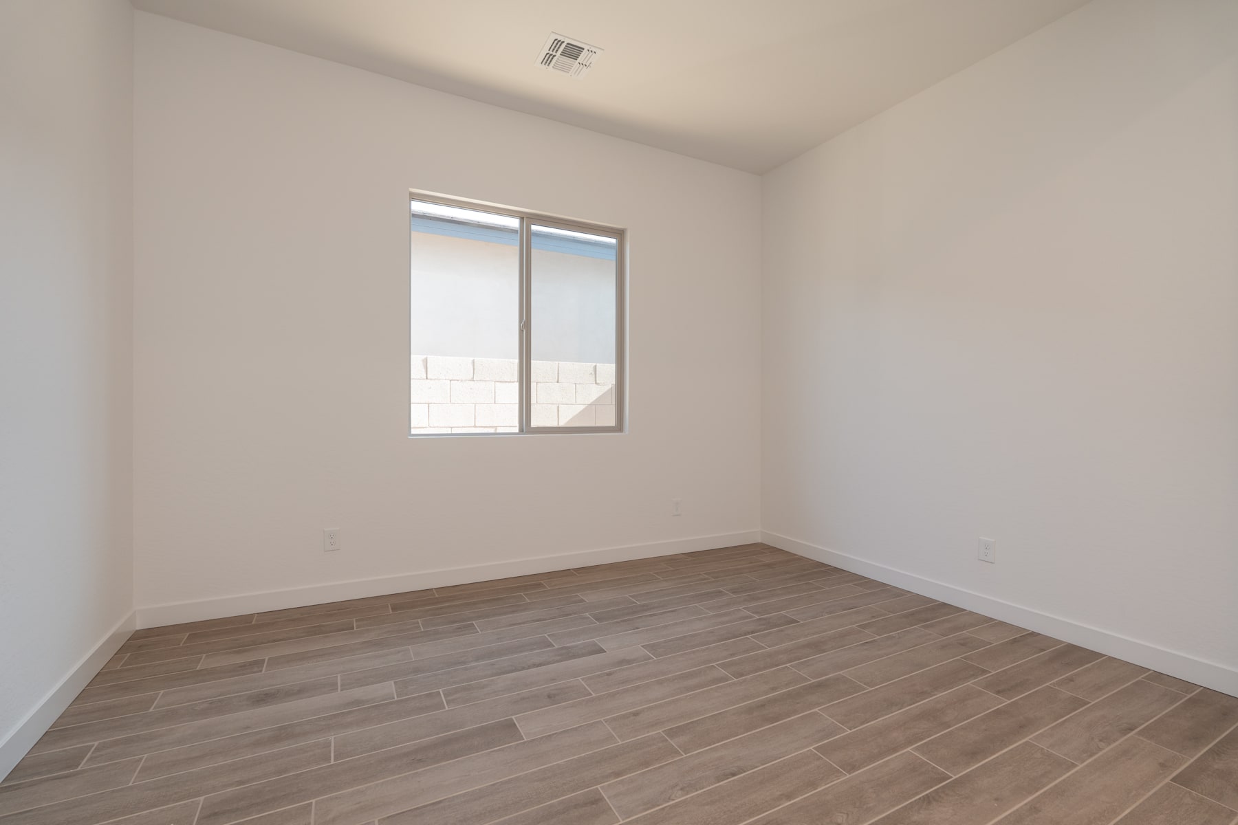 A simple, minimalist room with a window, hardwood-style flooring, and bare walls.