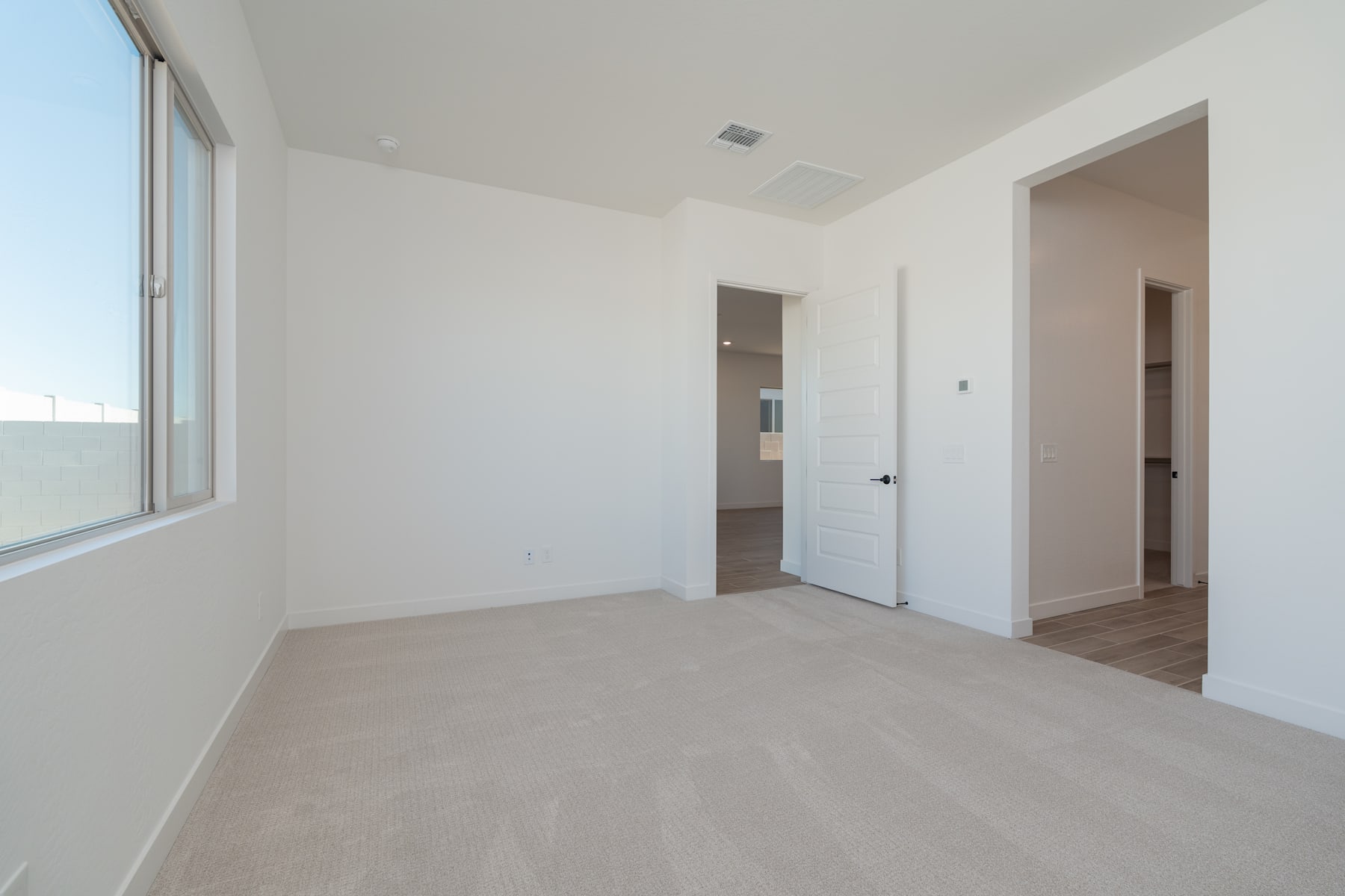 A spacious, minimalist room with a large window, hardwood floors, and a plain white wall.