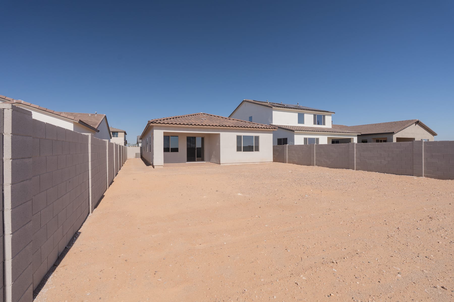 A residential neighborhood with newly constructed houses, surrounded by a sandy, unpaved area in the foreground.