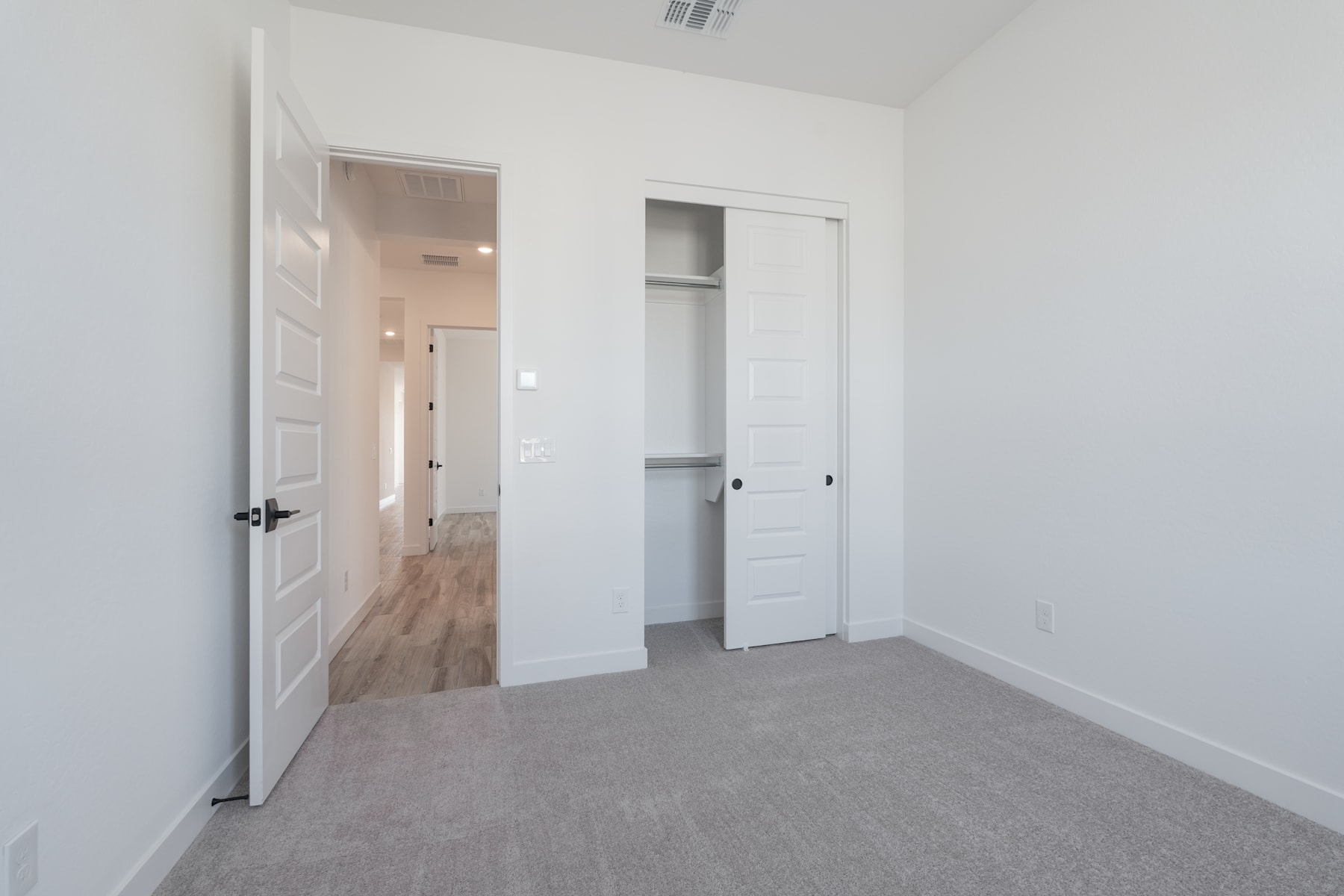 A spacious, minimalist room with white walls, a wooden floor, and a closet door visible in the background.
