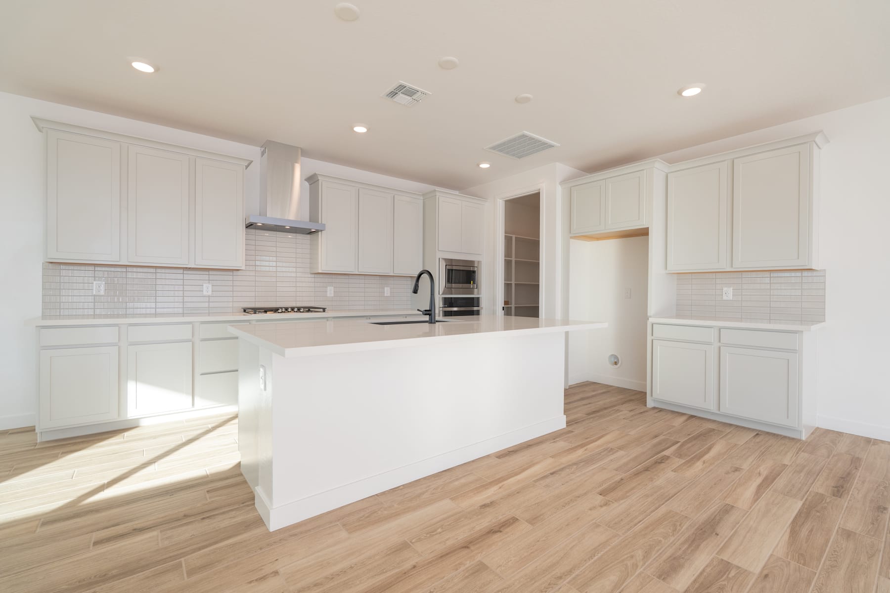 A modern, bright kitchen with white cabinets, a central island, and hardwood floors.