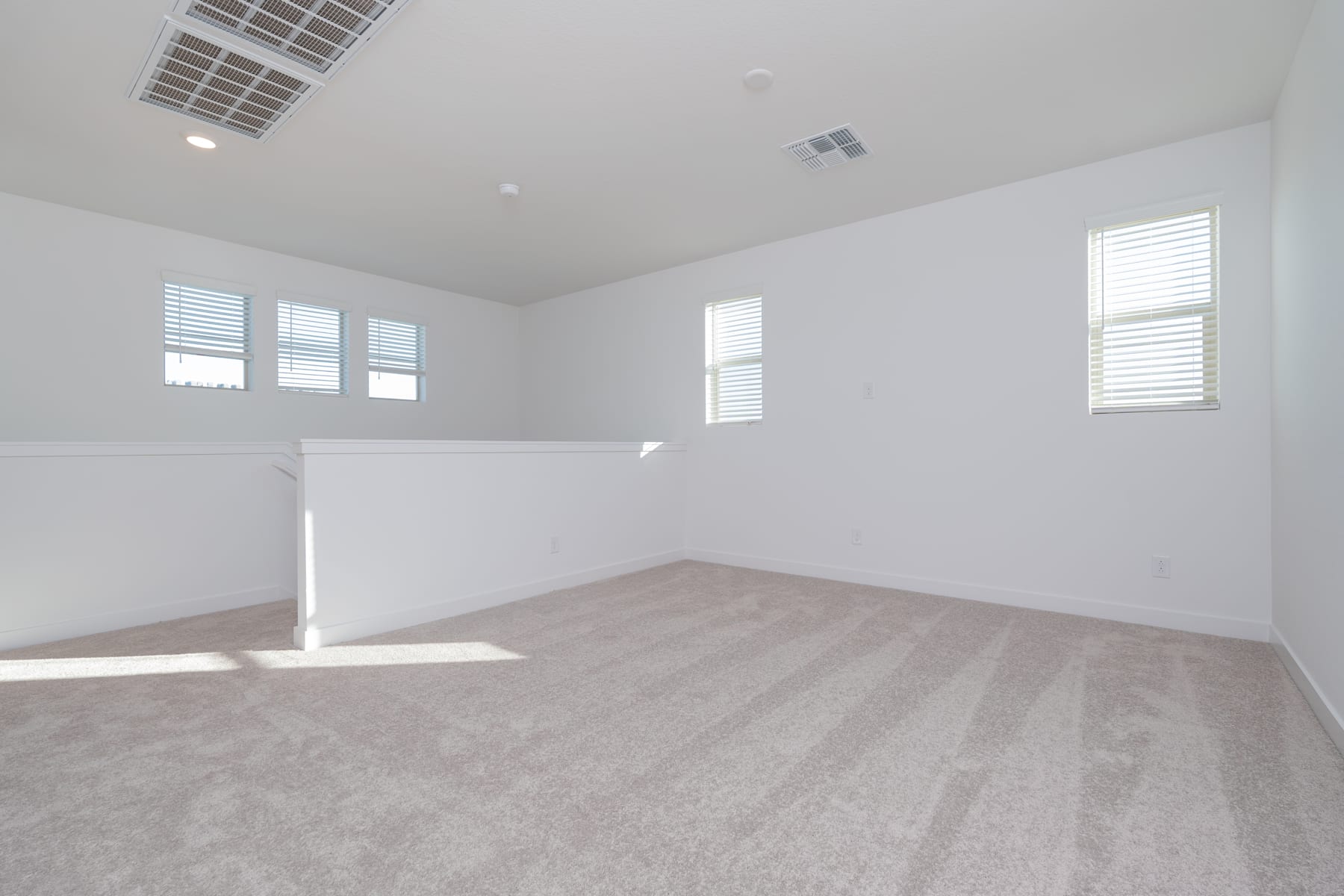 A bright, spacious room with white walls, hardwood floors, and large windows allowing natural light to flood the space.
