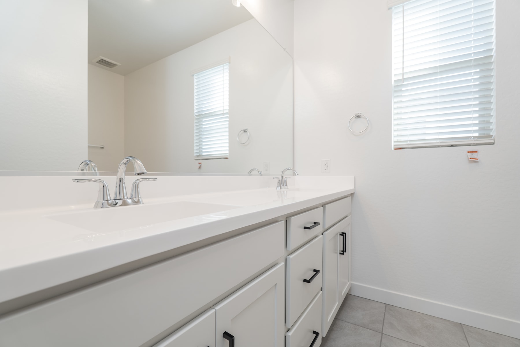 A modern, minimalist bathroom with a white vanity, double sinks, and a large window providing natural light.