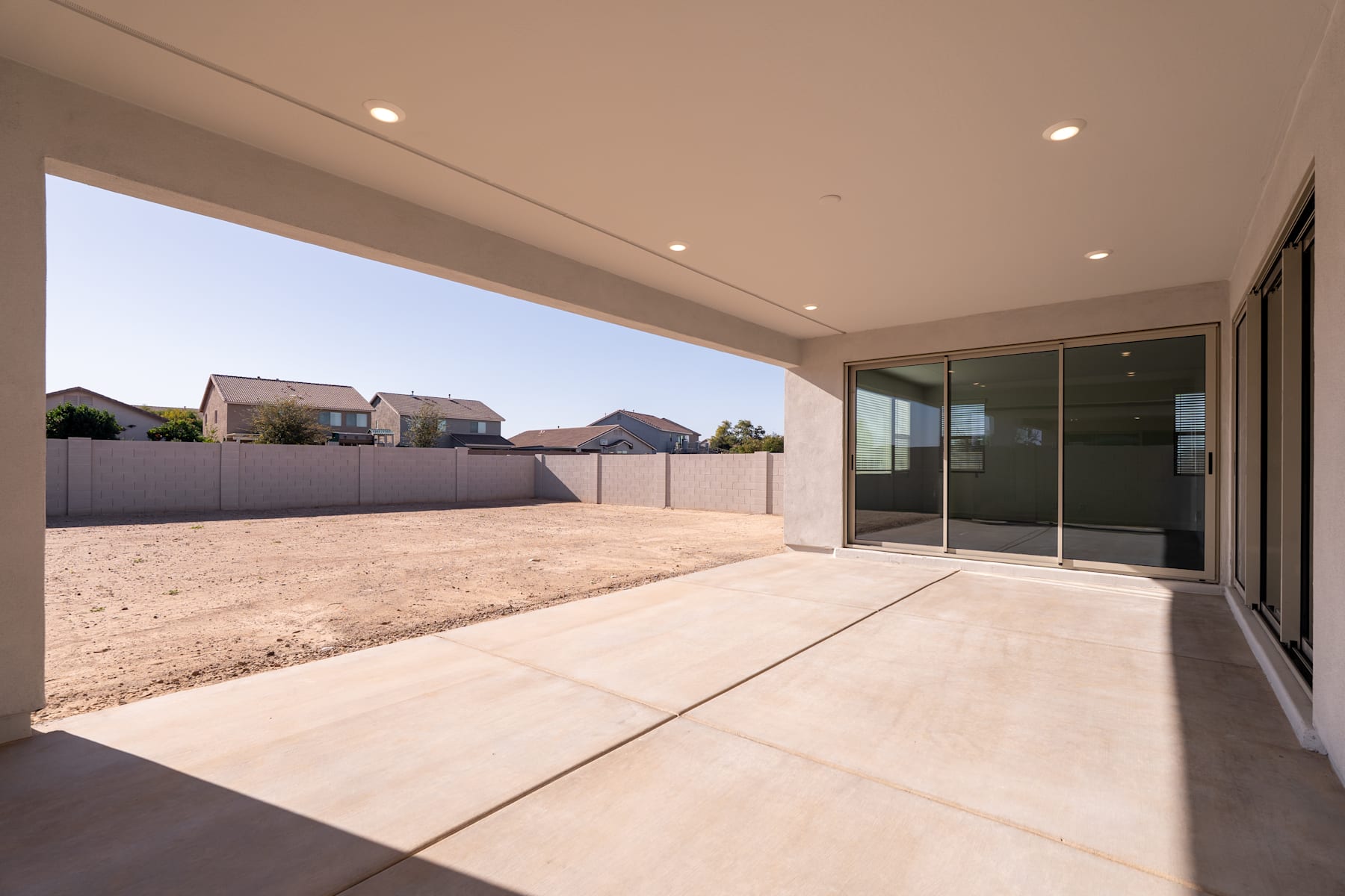 A spacious outdoor patio with a concrete floor, surrounded by a fence and neighboring houses in the background.