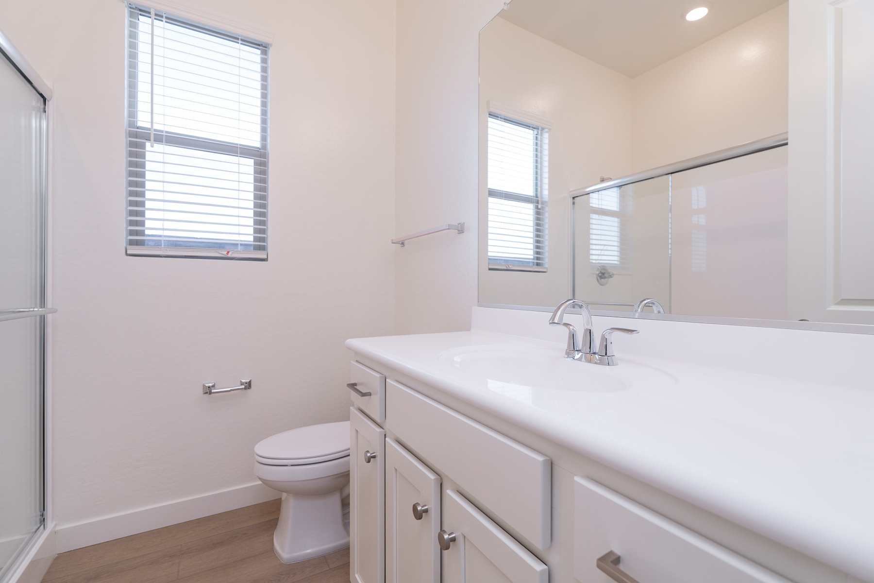 A modern, well-lit bathroom with a white vanity, a toilet, and a large window providing natural light.