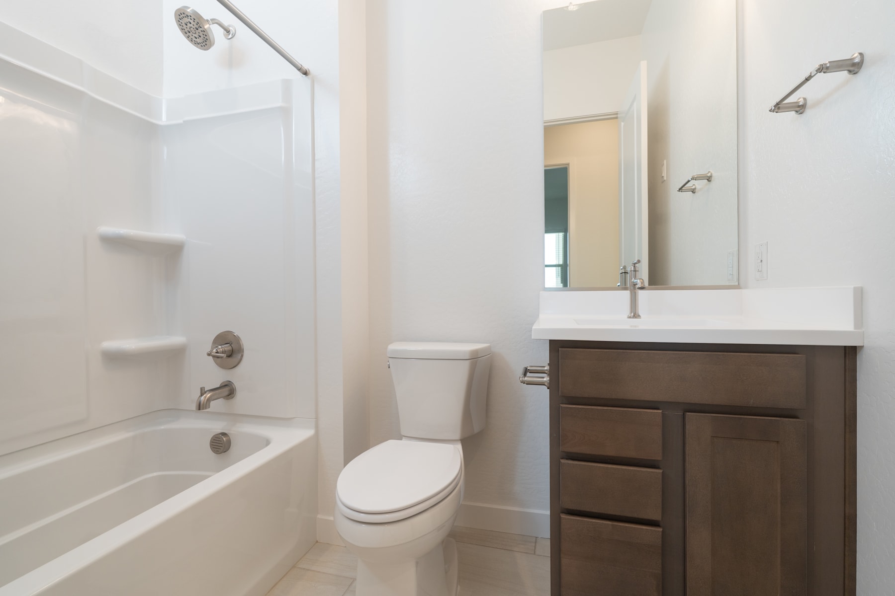 A modern bathroom with a white tiled wall, a bathtub, a toilet, and a wooden vanity cabinet with a sink and mirror.