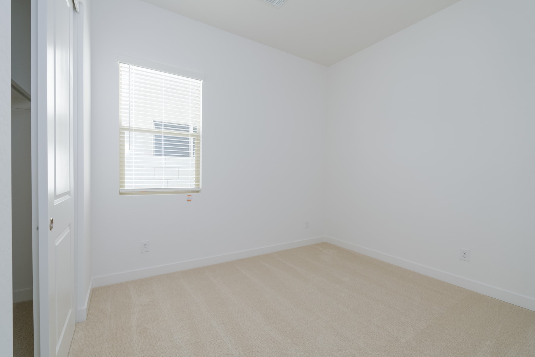 A simple, minimalist room with a single window, white walls, and a light-colored hardwood floor.