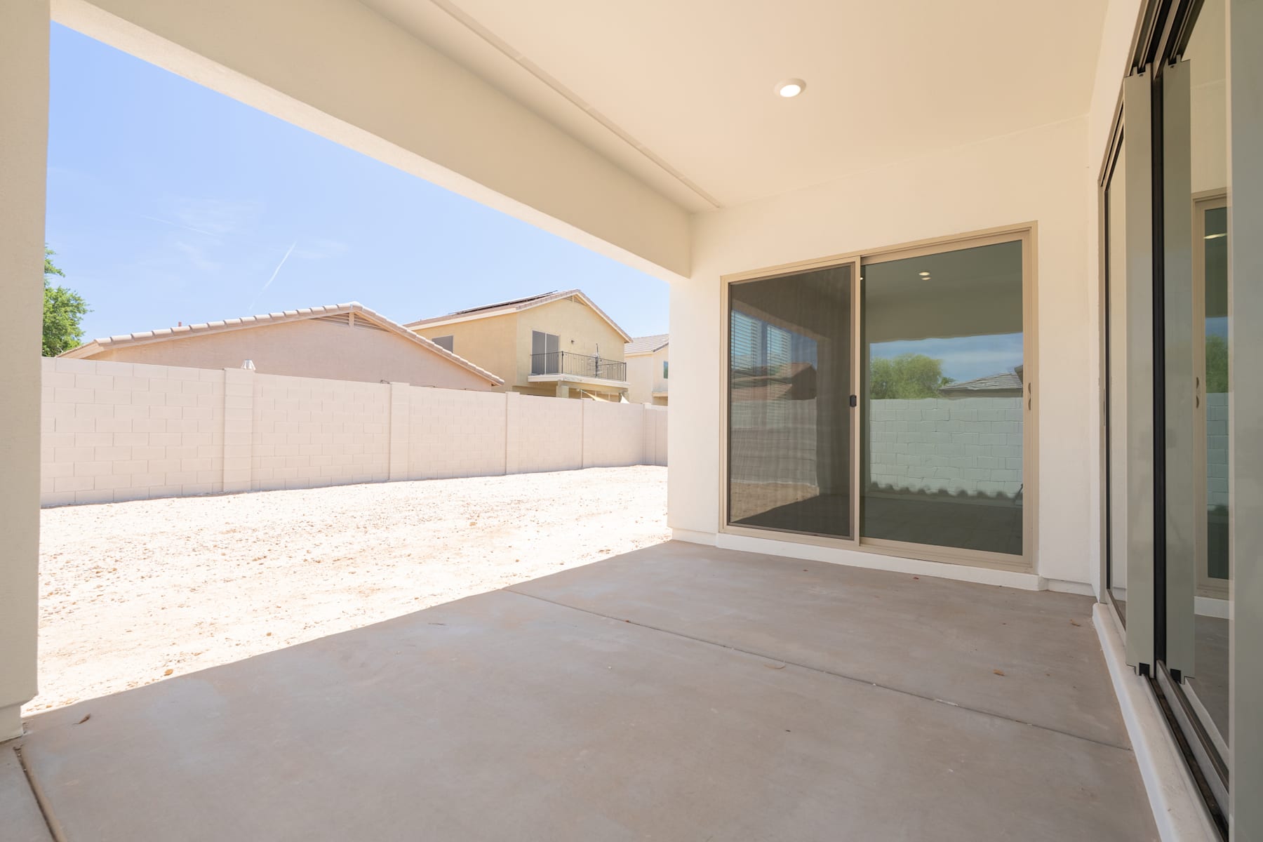 A spacious outdoor patio with a concrete floor, surrounded by a white wall and neighboring buildings, with a clear blue sky visible in the background.