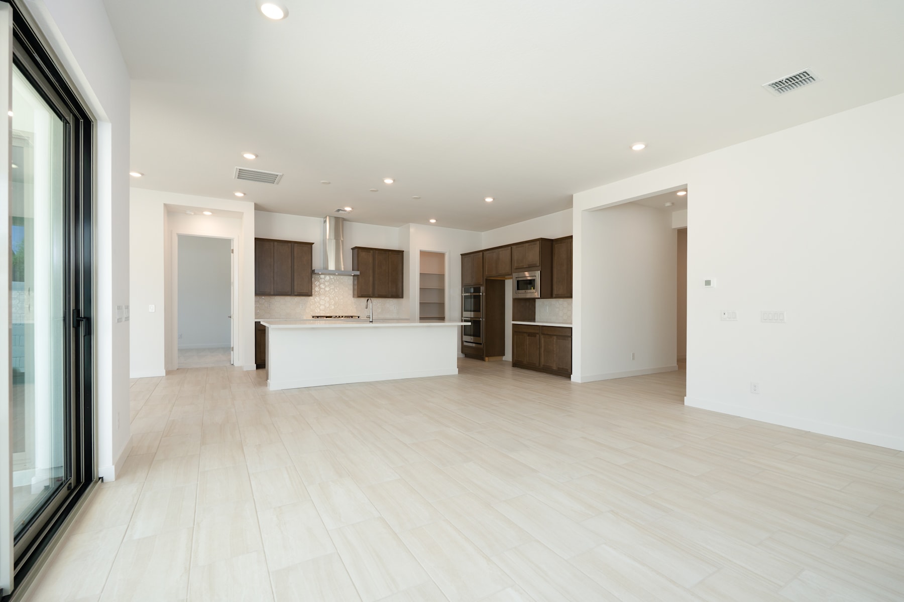 A spacious, modern kitchen with dark wood cabinets, a white countertop, and a large sliding glass door leading to an open living area with a hardwood floor.