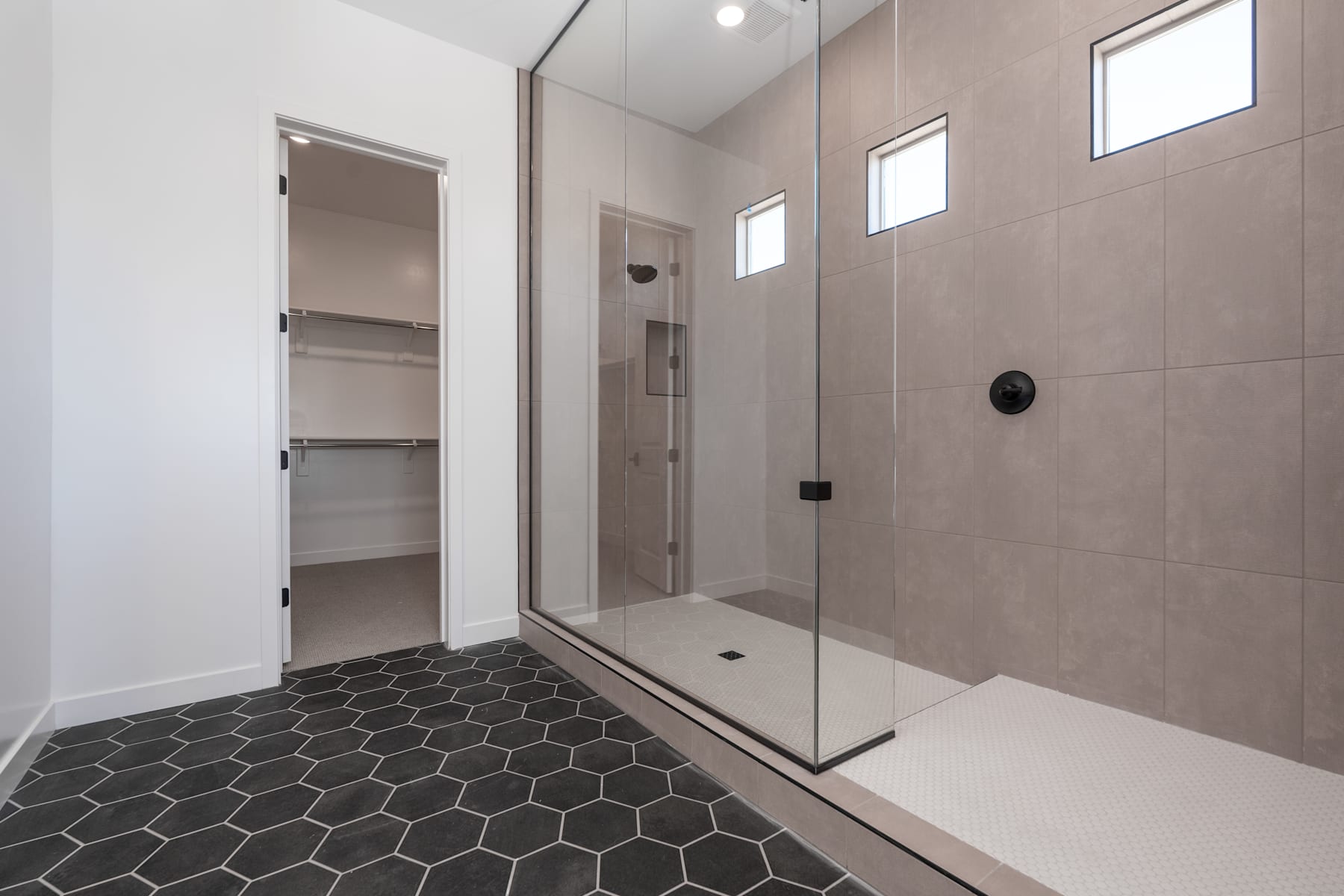 A modern and minimalist bathroom with a large walk-in shower, a built-in storage cabinet, and a hexagonal tile floor.