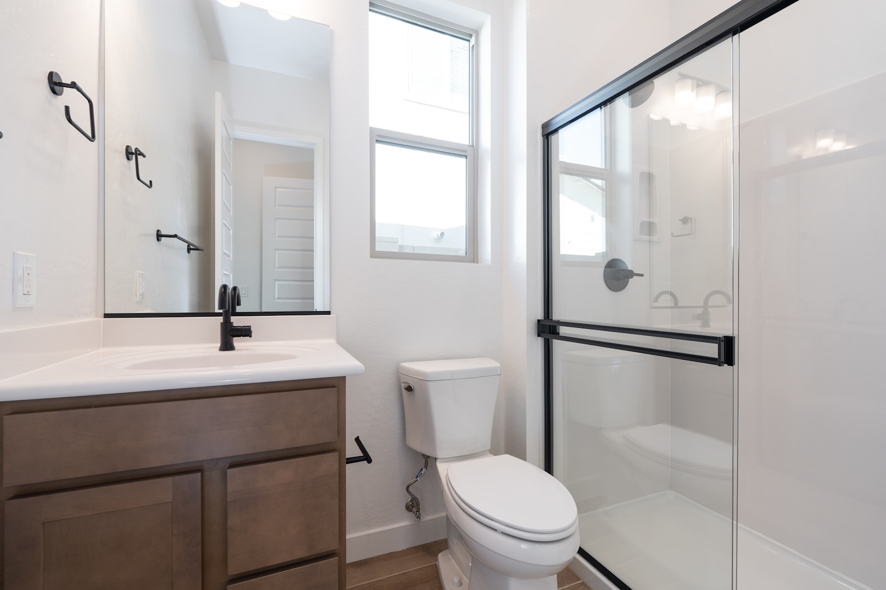 A modern, minimalist bathroom with a vanity, toilet, and glass-enclosed shower, illuminated by natural light from a large window.