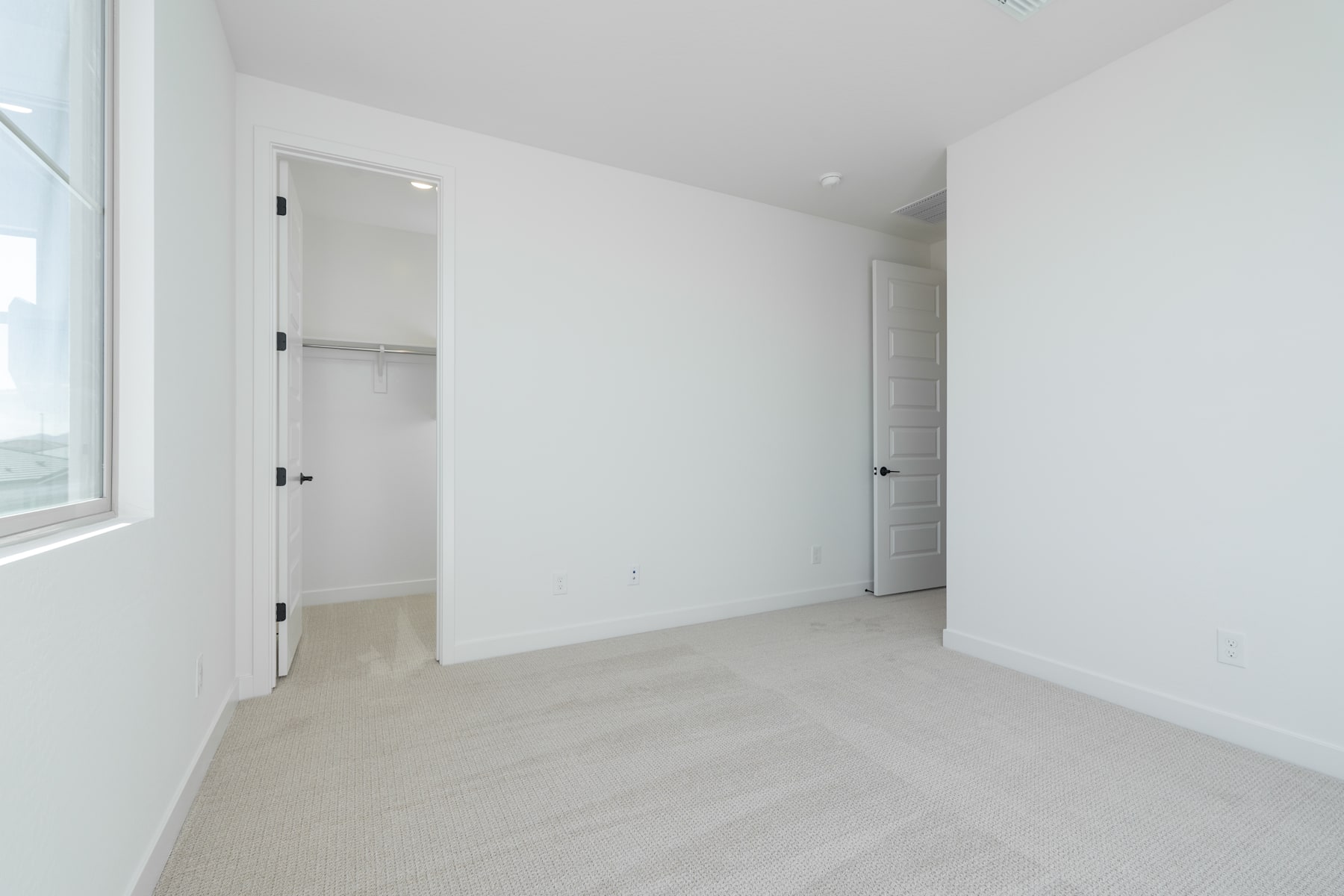A simple, minimalist bedroom with white walls, a window, and a closet door visible.