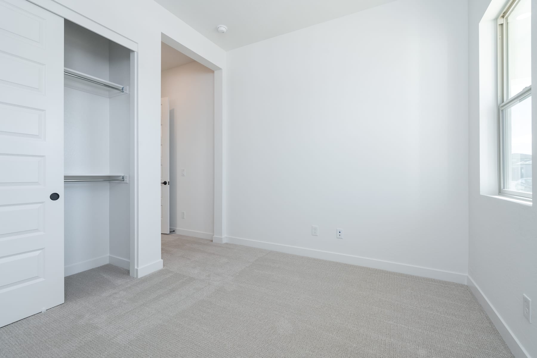A bright, minimalist bedroom with a closet and a window, featuring light-colored walls and floors.