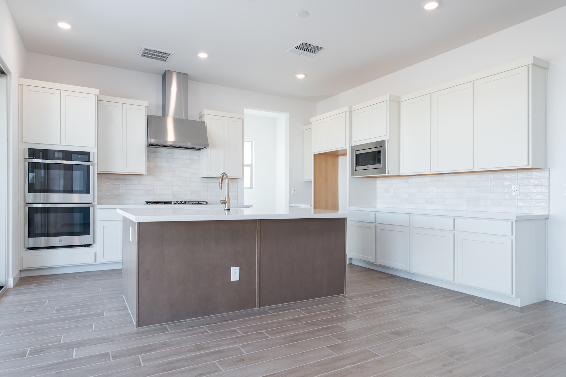 A modern, open-concept kitchen with white cabinets, a central island, and hardwood flooring.