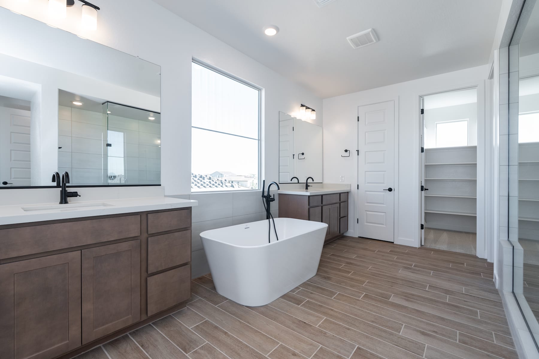 A modern and spacious bathroom with a freestanding bathtub, double vanity, and tiled flooring, all in a neutral color palette.