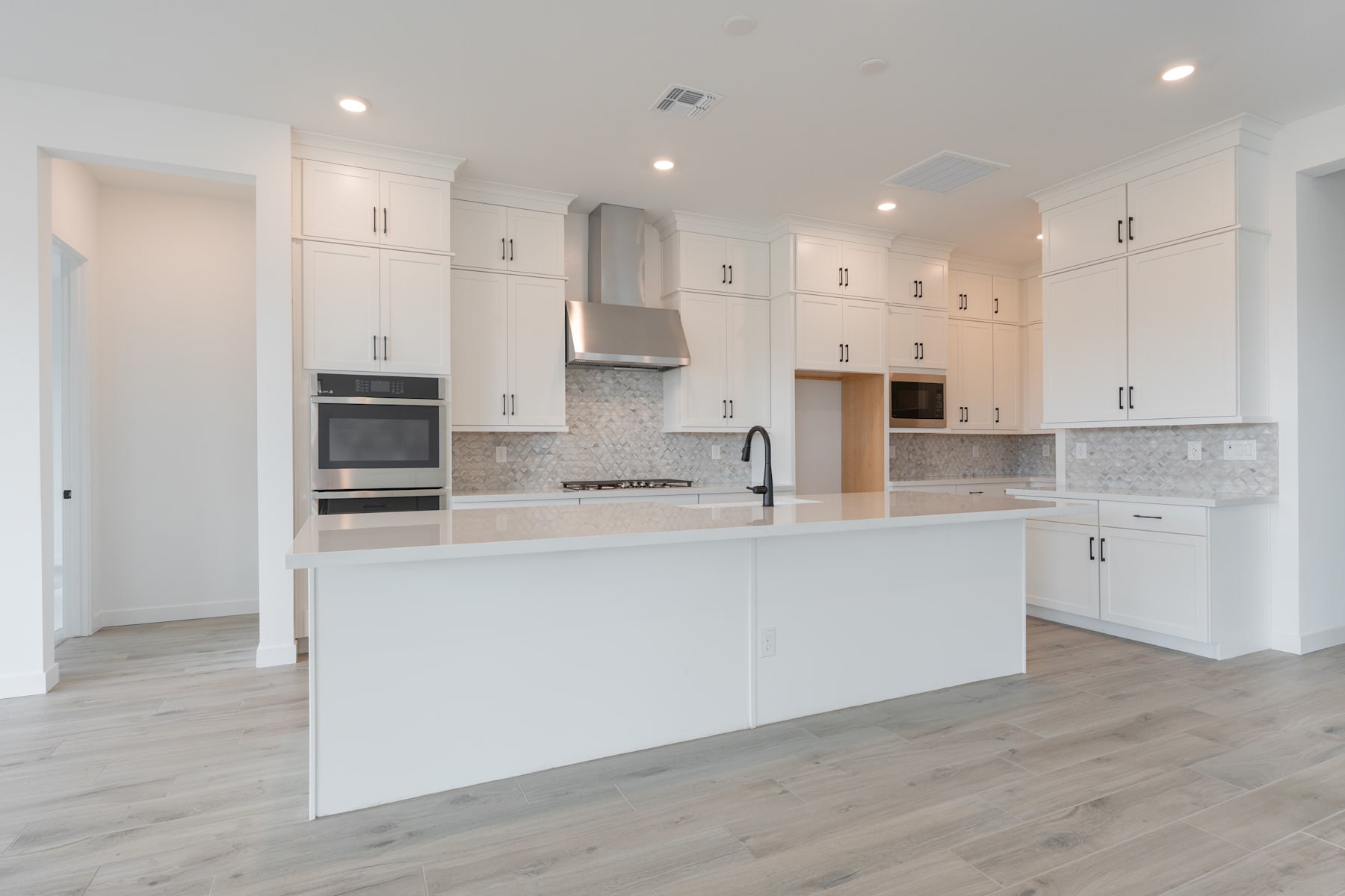 A modern, bright, and spacious kitchen with white cabinets, a central island, and hardwood floors.