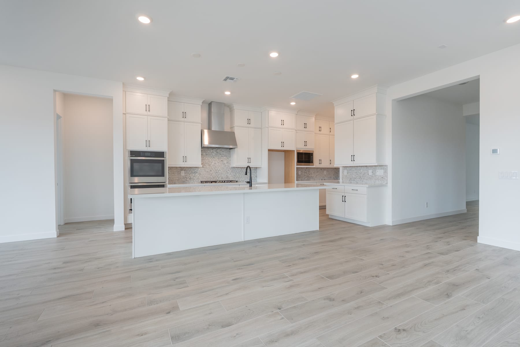A modern, open-concept kitchen with white cabinets, stainless steel appliances, and a hardwood floor that extends throughout the space.