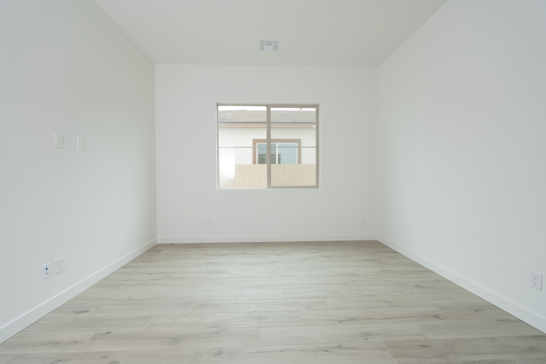 A bright, minimalist room with white walls and a wooden floor, featuring a window that allows natural light to fill the space.