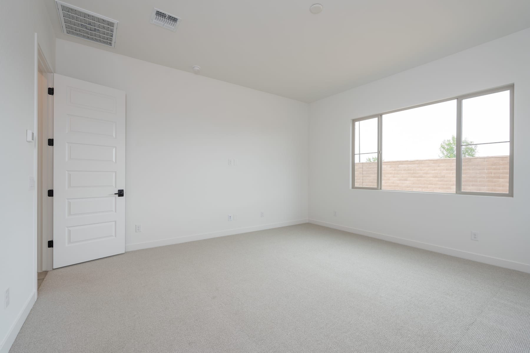 A spacious, minimalist room with white walls, a white door, and a large window providing natural light.