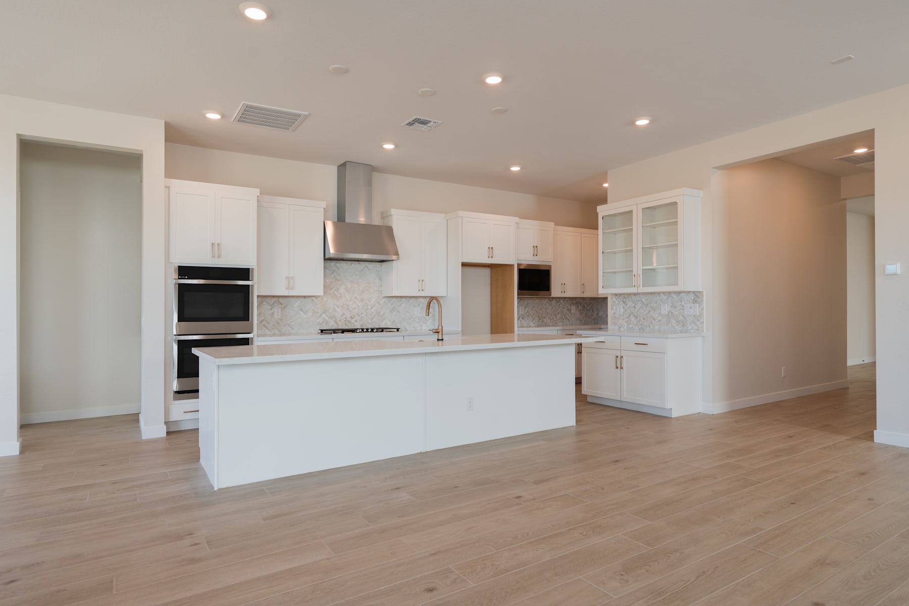 A modern, open-concept kitchen with white cabinets, stainless steel appliances, and a central island on a hardwood floor.