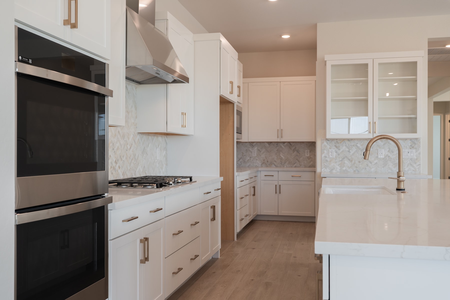 A modern, well-equipped kitchen with white cabinets, stainless steel appliances, and a tiled backsplash, set against a hardwood floor.
