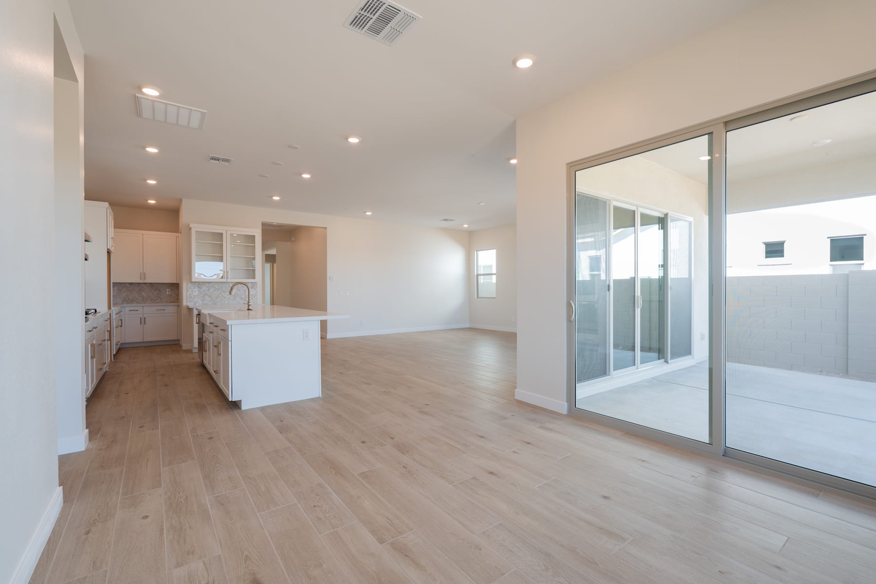 A spacious, well-lit room with a modern kitchen, hardwood floors, and sliding glass doors leading to an outdoor area.