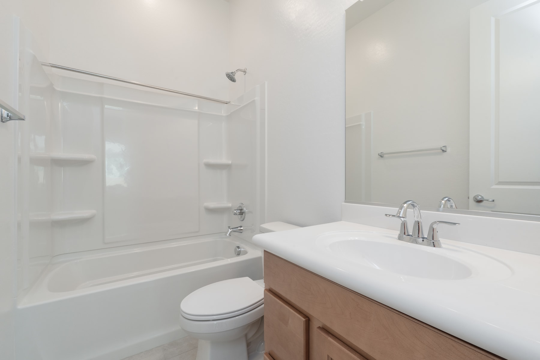 A modern, minimalist bathroom with a white vanity, a toilet, and a bathtub surrounded by white walls and shelving.
