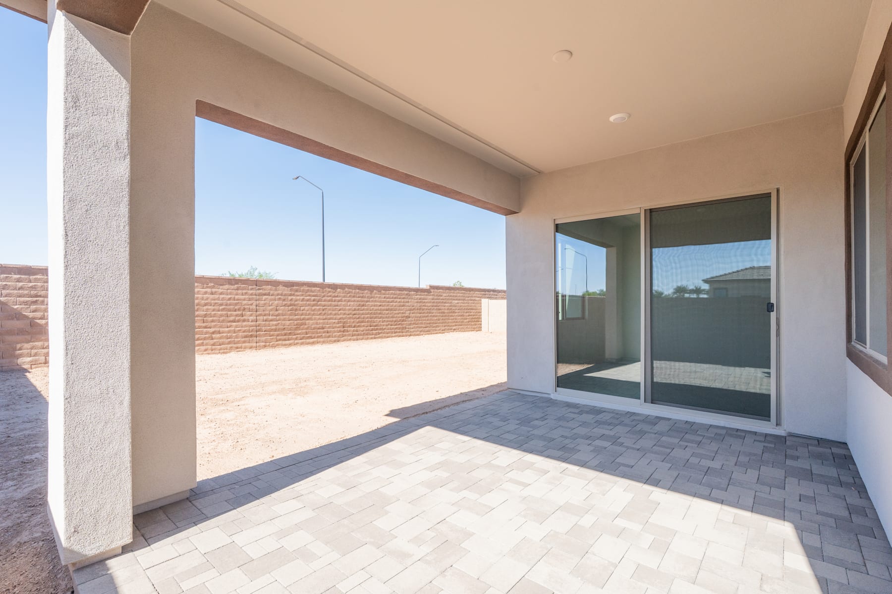 The image shows a spacious outdoor patio area with a tiled floor, large windows, and a brick wall in the background.