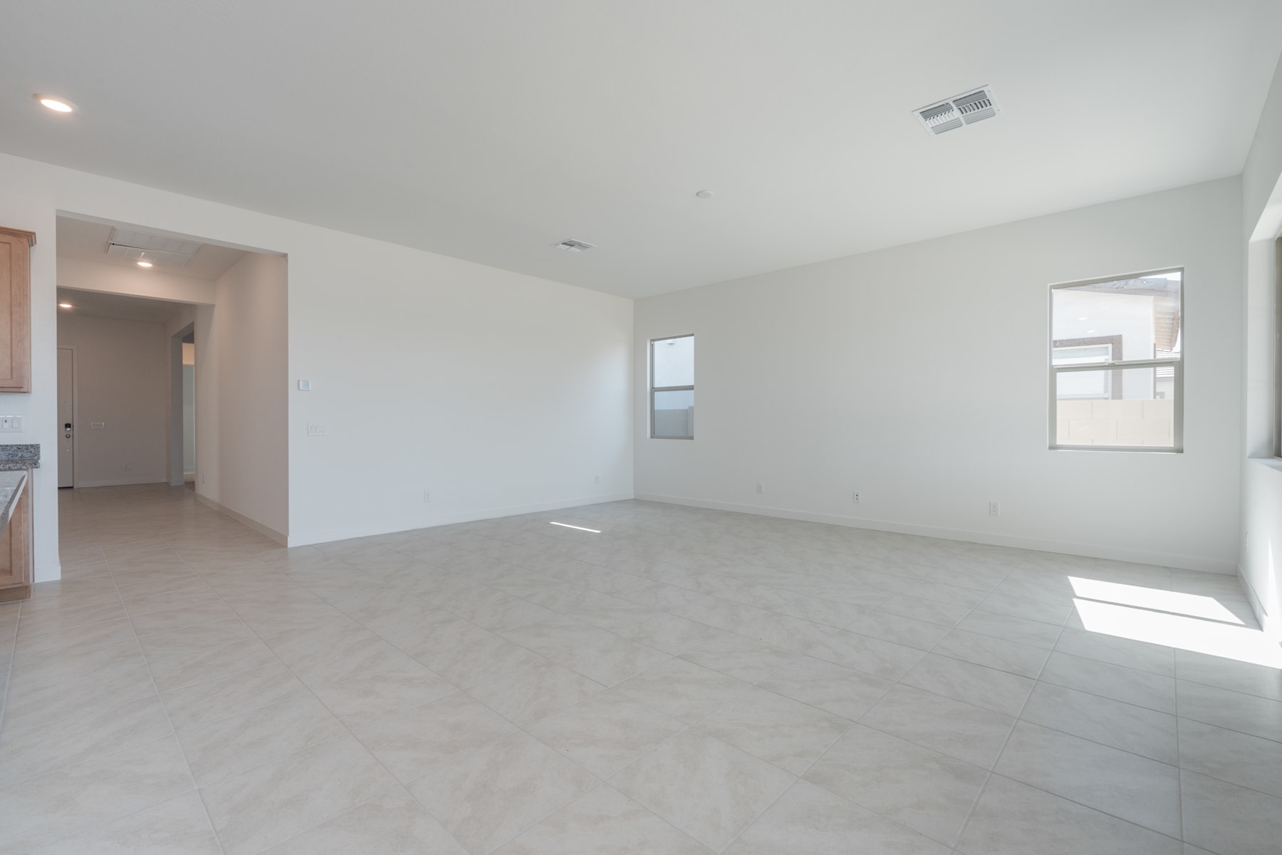 An empty, spacious room with white walls, a light-colored floor, and a window providing natural light.