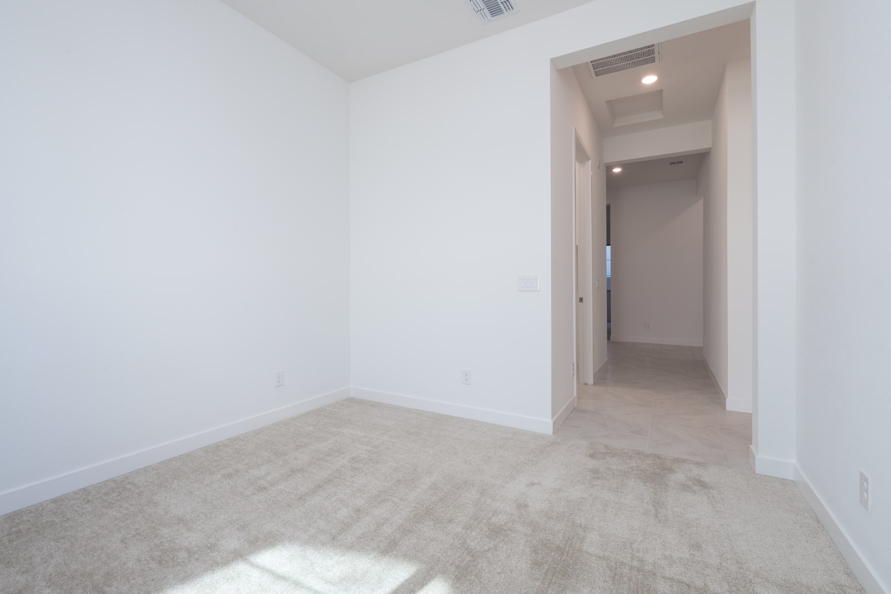 A spacious, empty room with white walls and a carpeted floor, leading to an open doorway in the background.