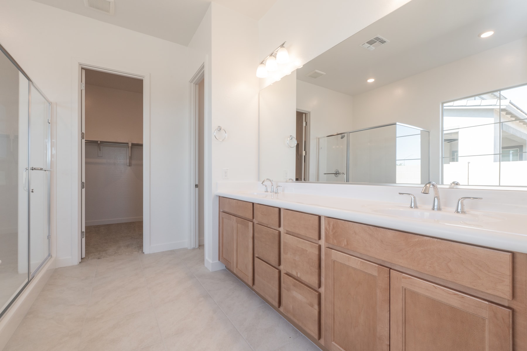 A spacious bathroom with a large vanity, double sinks, and a mirror on the wall, leading to an adjacent room.