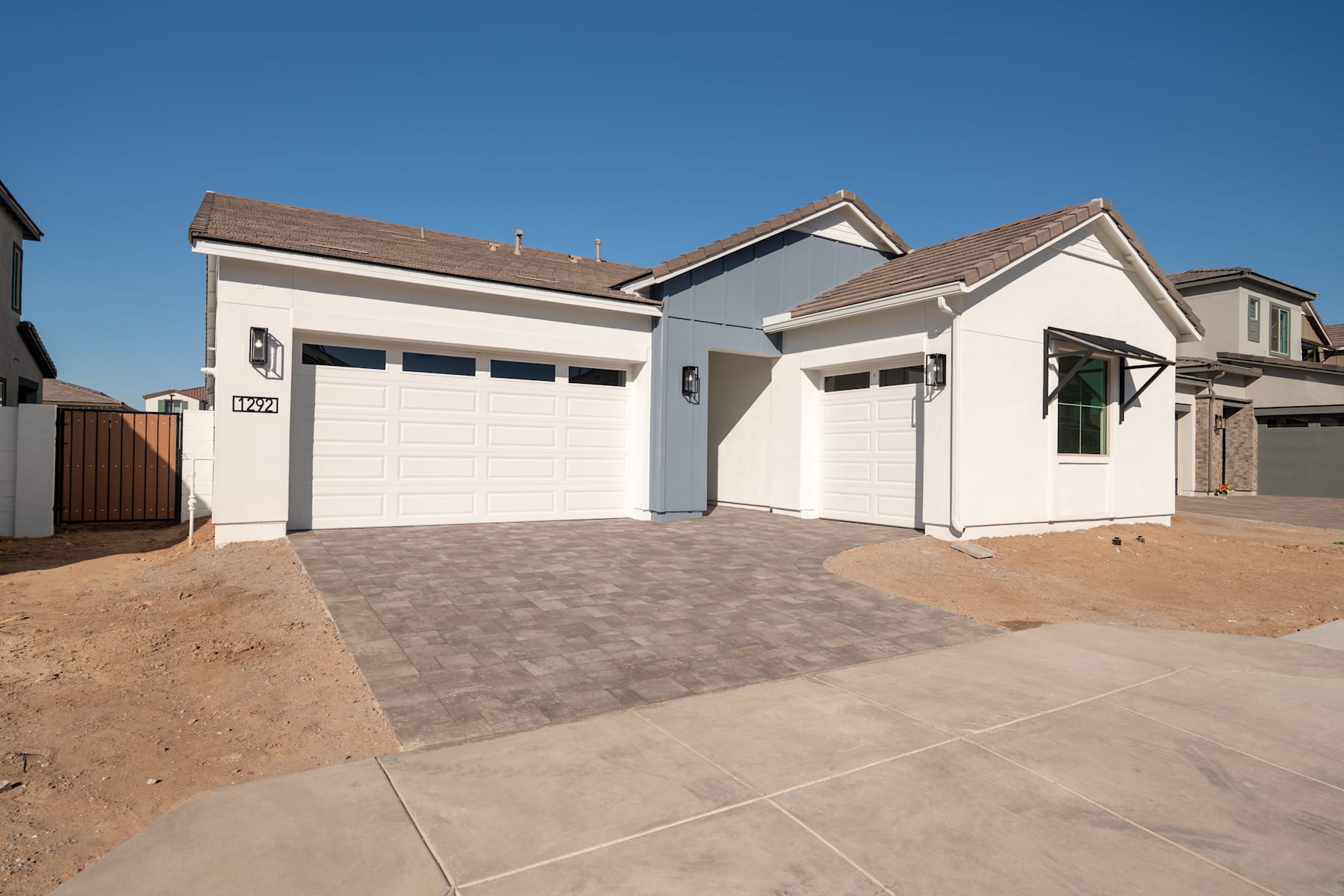 A modern, two-story residential home with a driveway and a paved walkway leading to the front entrance, set against a clear blue sky.