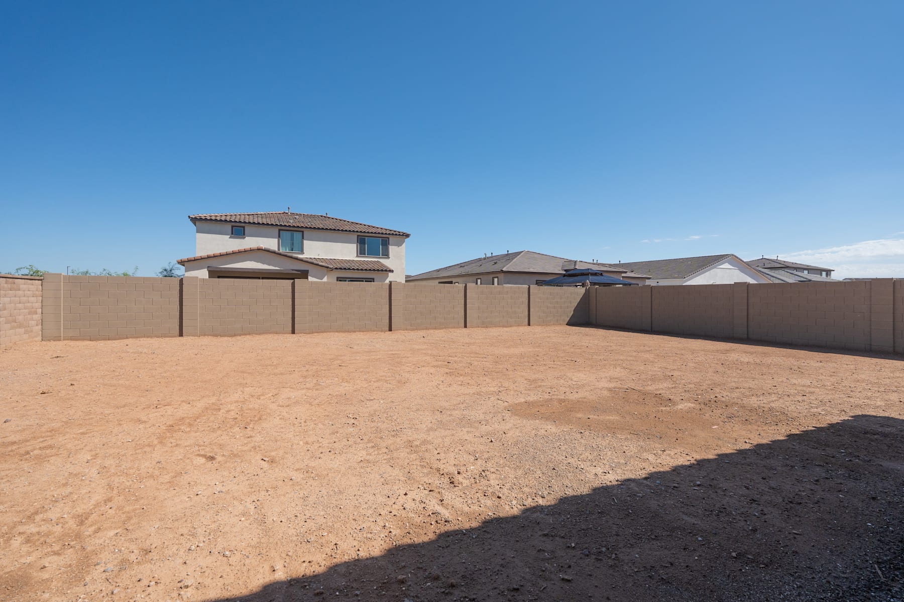 A large, open dirt lot with a two-story residential building in the background, surrounded by a fence.