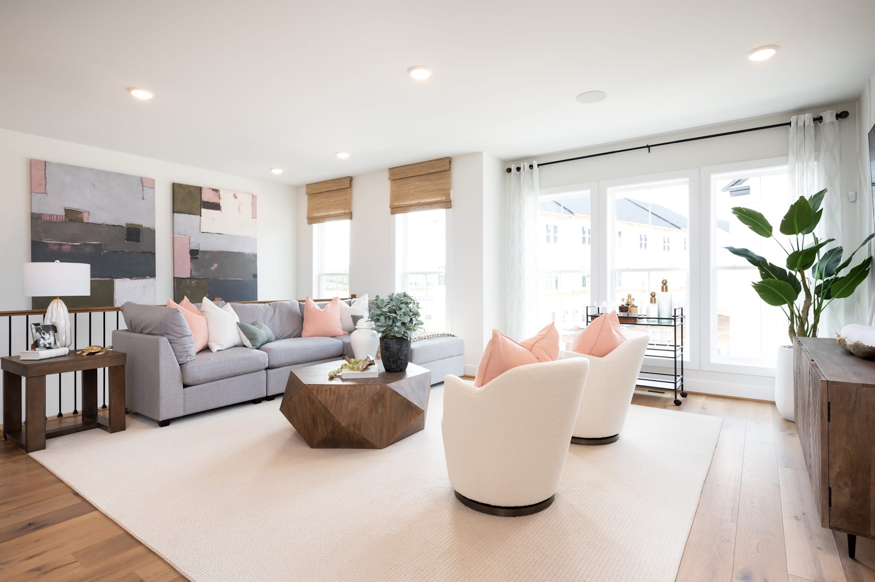 A modern and stylish living room with a gray sofa, white armchairs, and a wooden coffee table, surrounded by large windows that let in natural light and provide a view of the outdoors.