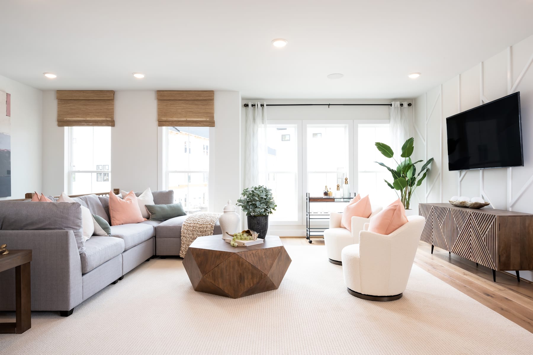 A cozy and modern living room with a gray sectional sofa, wooden coffee table, and a large window providing natural light, along with various decorative elements such as plants and artwork.