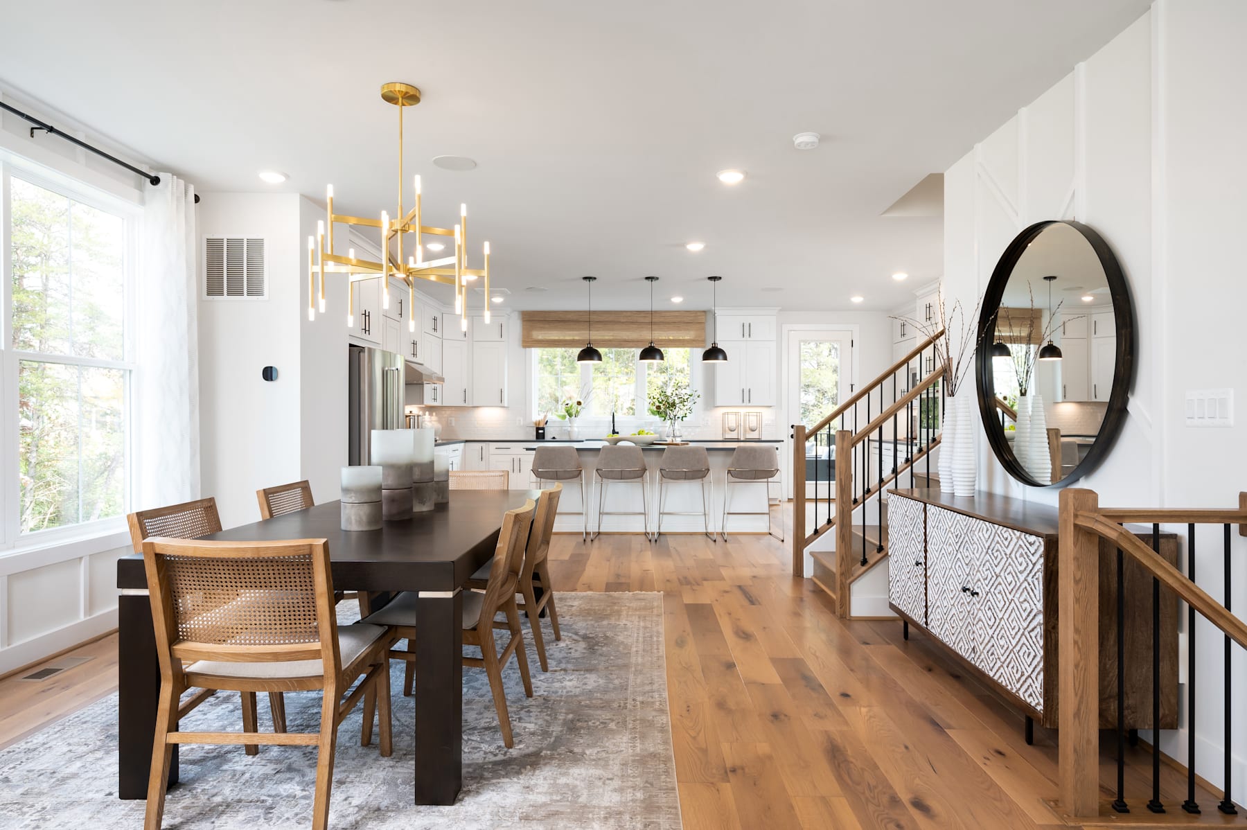 A spacious and well-lit open-concept kitchen and dining area with a wooden dining table, chairs, and a large mirror on the wall.