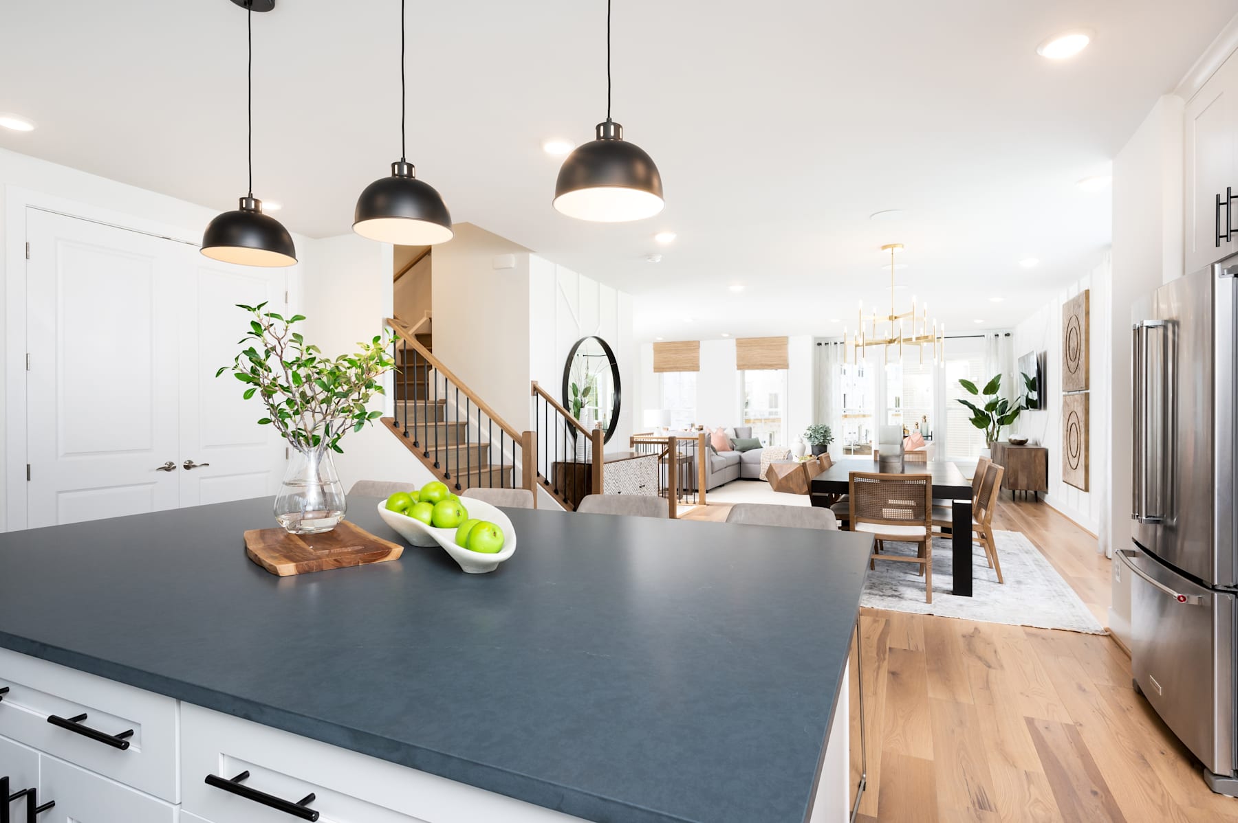 A modern and stylish kitchen with a dark countertop, pendant lights, and a view of a cozy living room in the background.