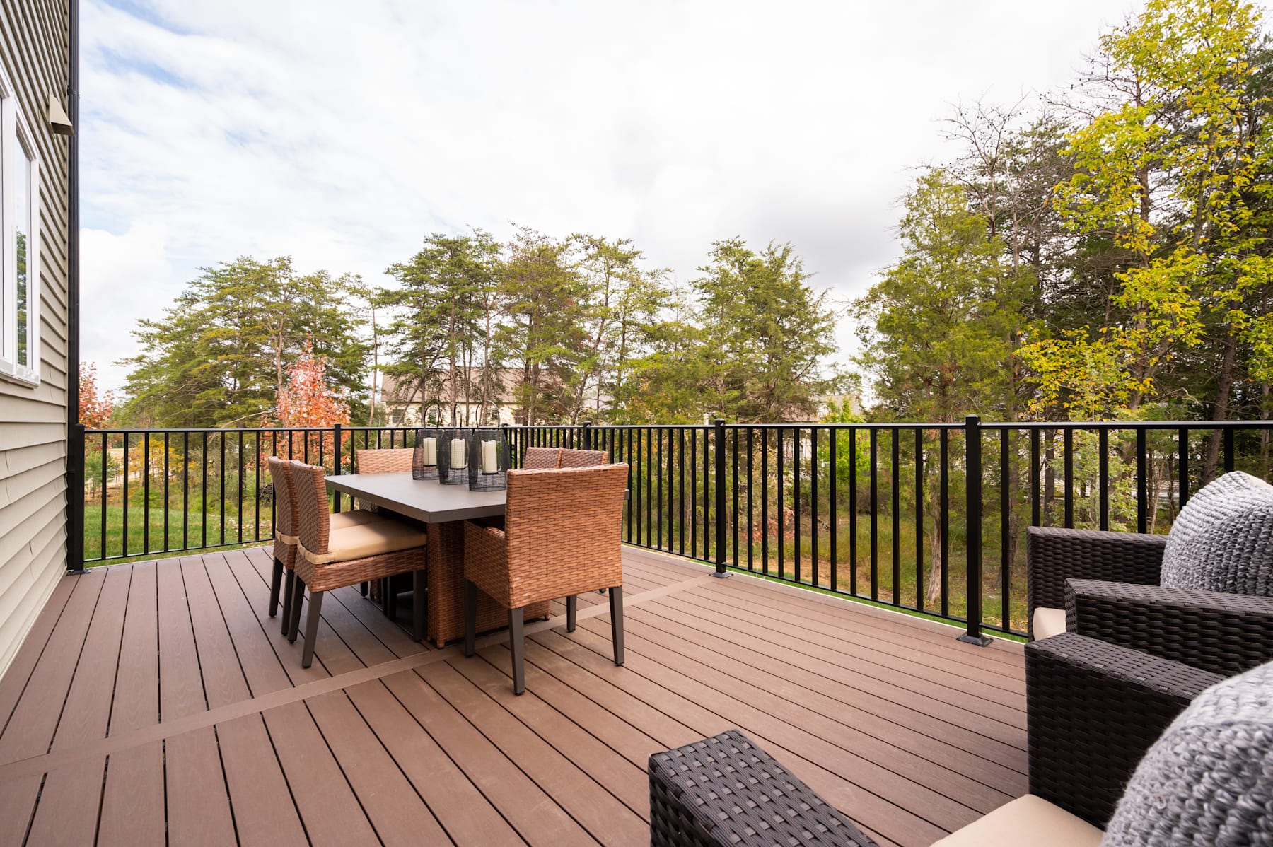 A wooden deck with a dining table and chairs overlooking a lush, forested landscape in the background.