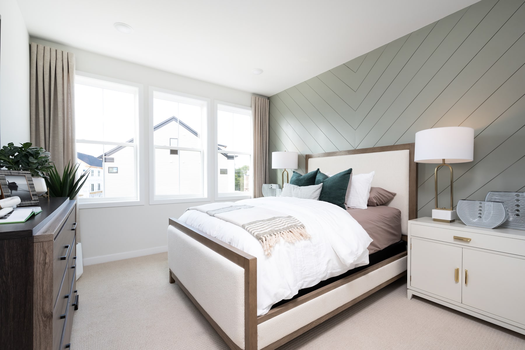 A cozy and modern bedroom with a large bed, neutral-toned walls, and a window providing natural light, along with various decorative elements and furniture pieces.