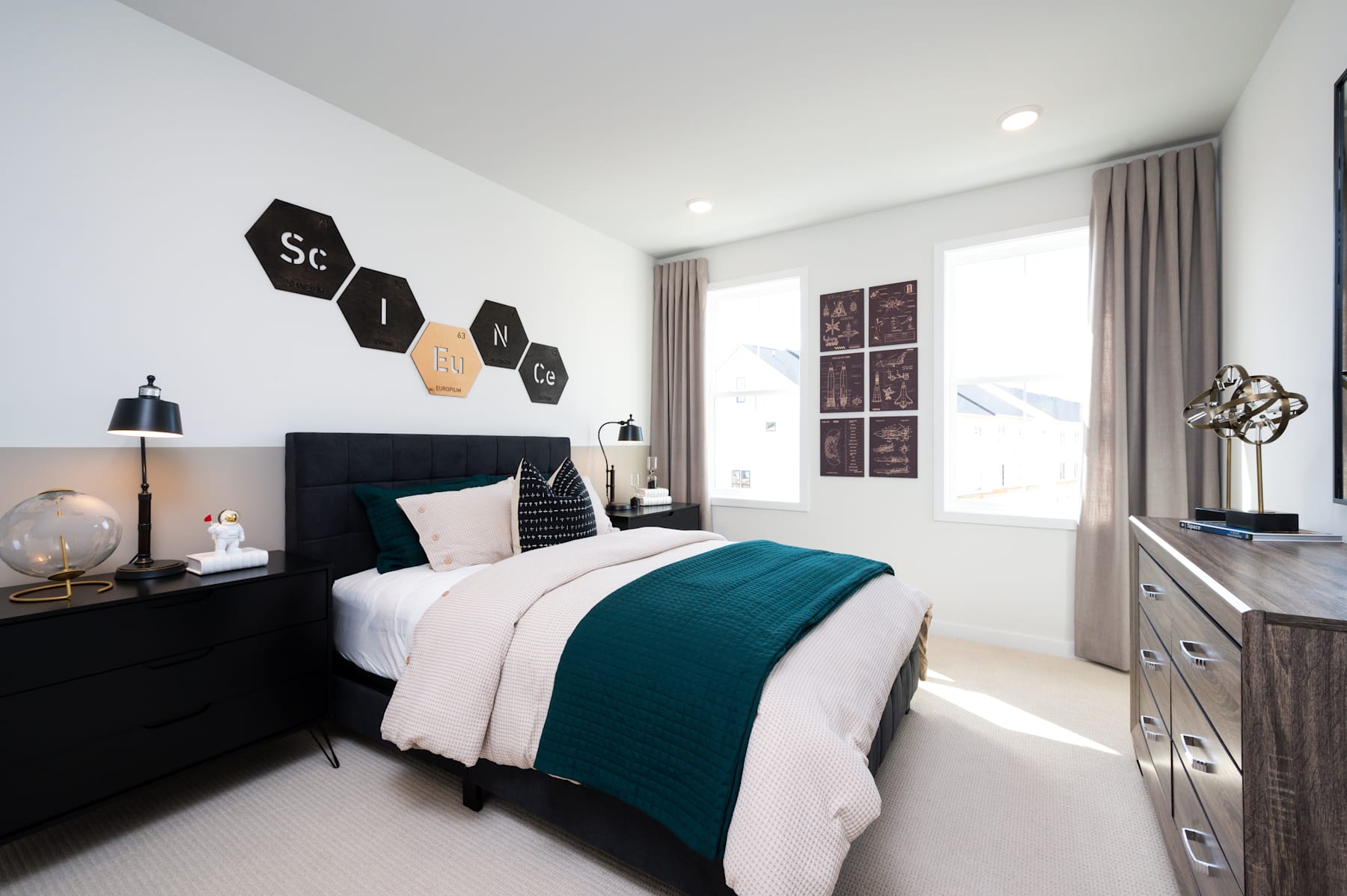 A modern and stylish bedroom with a black bed frame, white bedding, and teal accents, complemented by hexagonal wall decor and a dresser in the background.