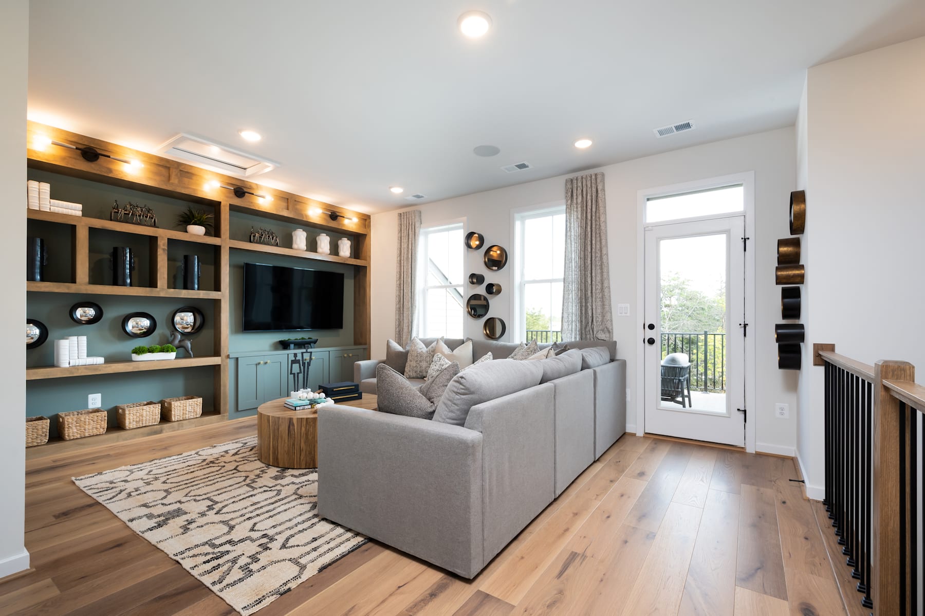 A cozy and well-designed living room with a gray sofa, wooden shelves, and a patterned rug on the hardwood floor, with a sliding glass door leading to an outdoor area.