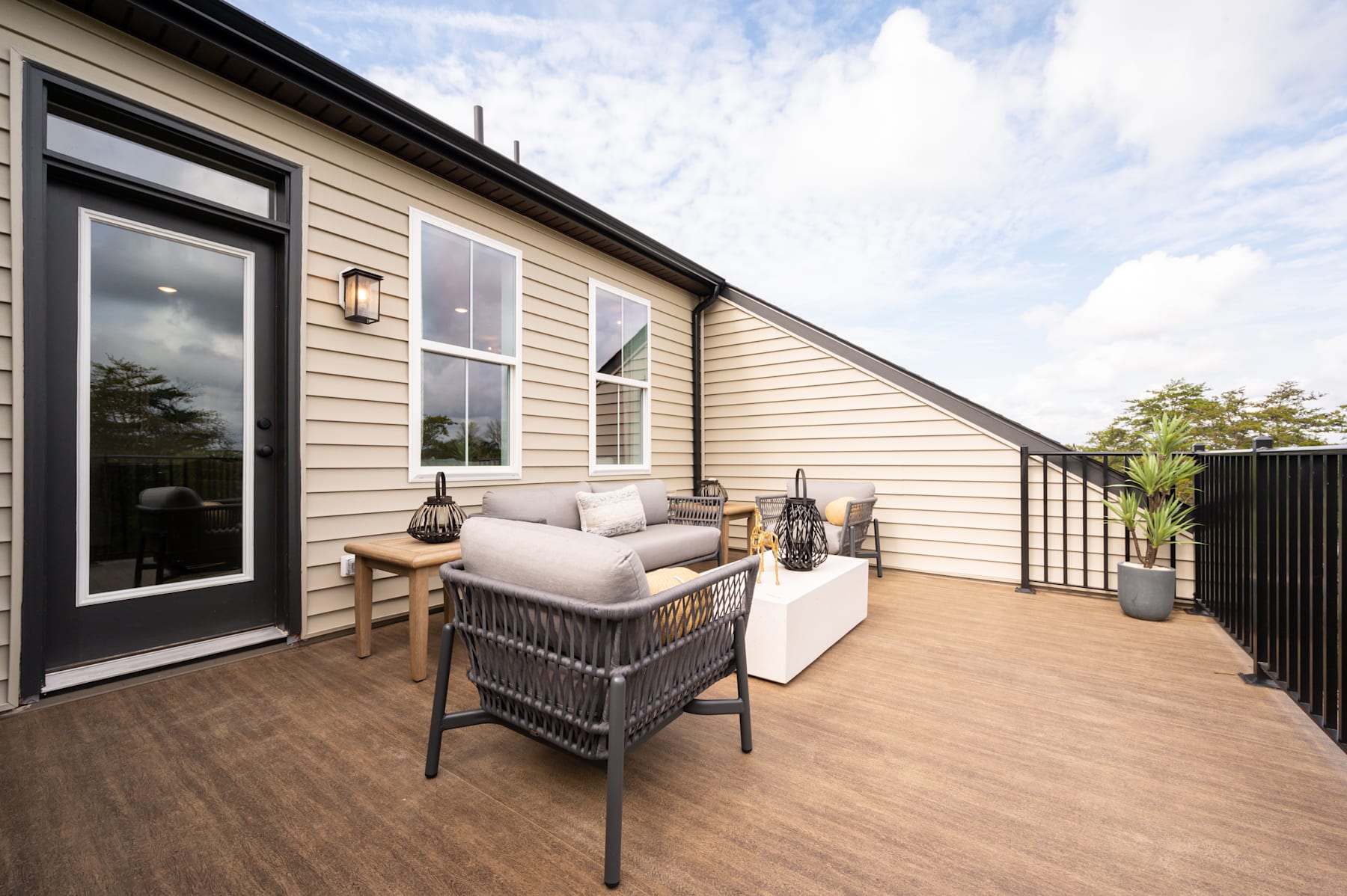 A cozy outdoor patio with comfortable seating, surrounded by a wooden structure and a scenic background with a cloudy sky.